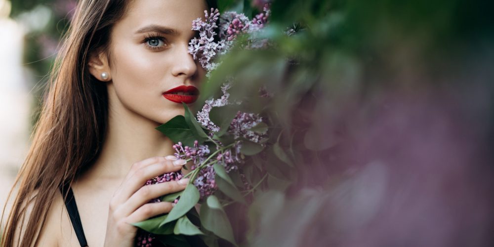 The charming girl stands near bushes with flowers