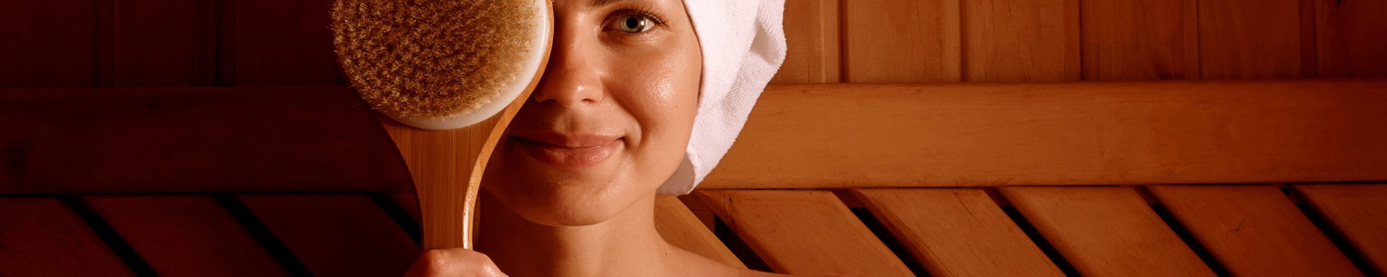 girl in a spa treatment in a traditional sauna with a brush for skin and a washcloth. relaxes wrapped in a white towel